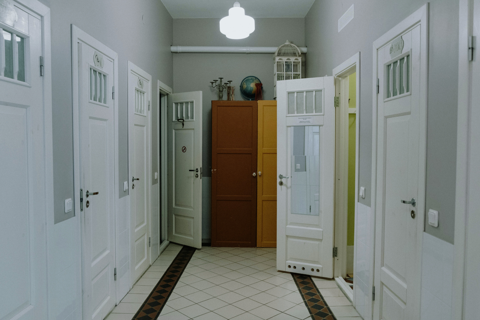 Interior hallway with multiple white panel doors, some open, showcasing different room layouts and lighting; includes colorful cabinets and decorative items at the end